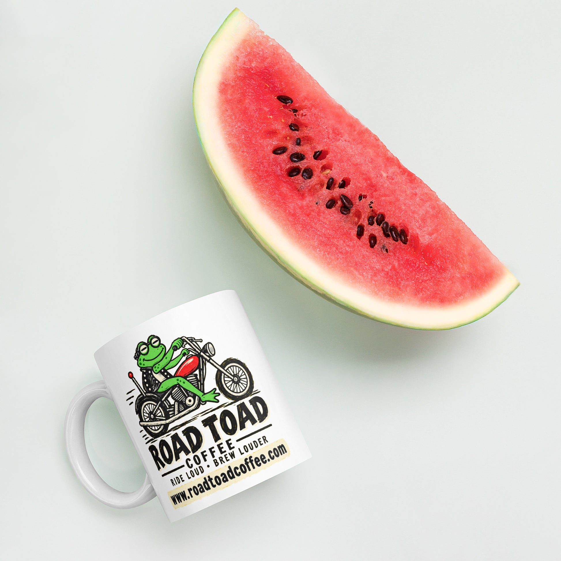 White 11 oz Road Toad Coffee mug with roadtoadcoffee.com next to watermelon